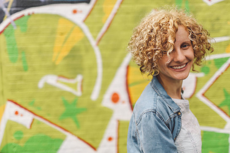 Portrait of happy woman against graffiti on wall