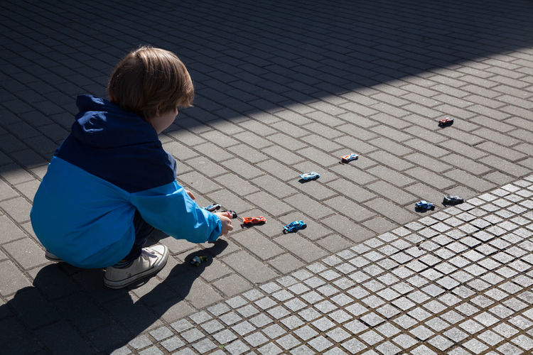 High angle view of boy playing with toy cars on footpath