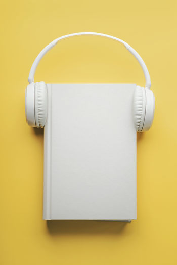 Directly above shot of headphones with book over yellow background