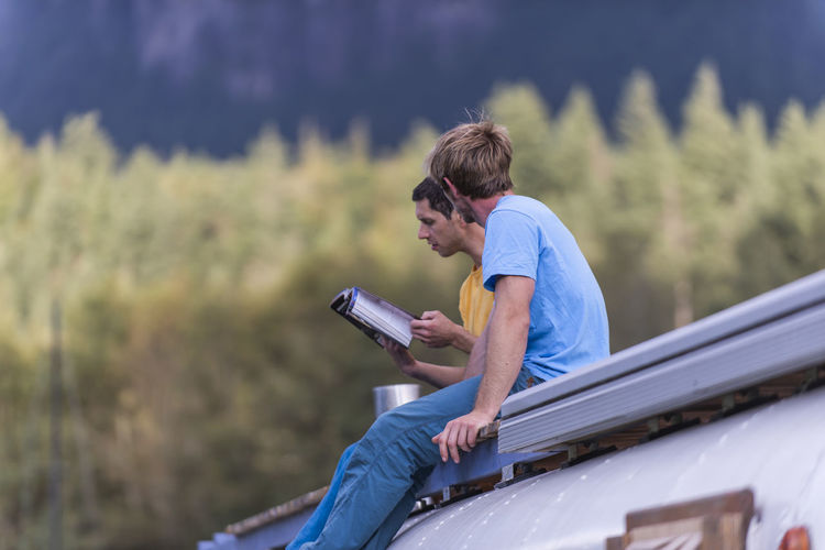 Two people sitting on roof top school bus reading climbing guidebook