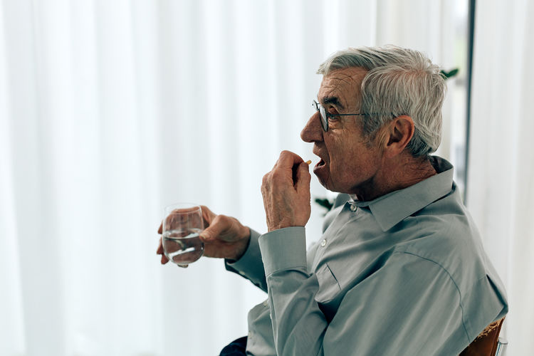 Old man taking pill. senior person holding a glass water ready to swallow medication.