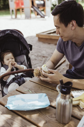 Father feeding male toddler while sitting in playground