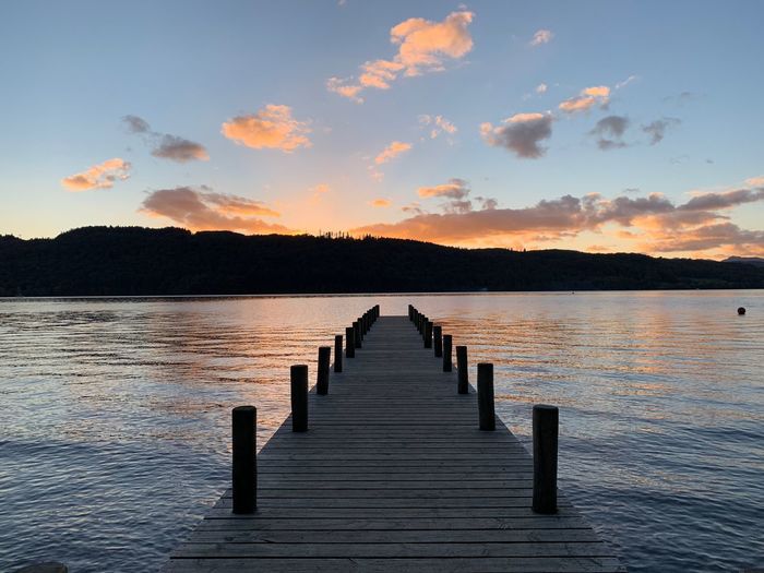 Wooden pier over lake against sky during sunset