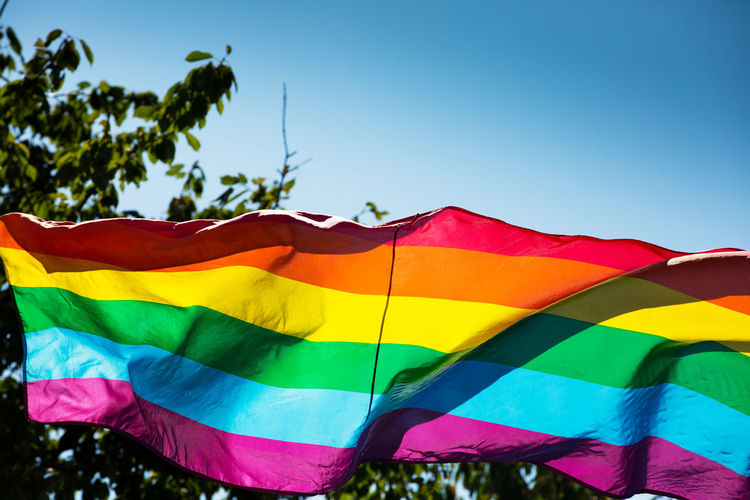 Low angle view of rainbow flag waving against clear blue sky