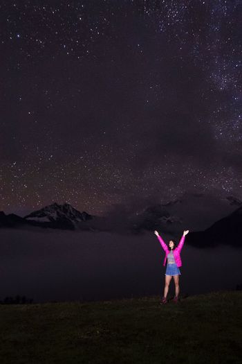 Rear view of woman doing yoga on field against sky at night