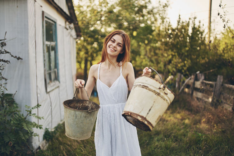 Smiling woman holding buckets while standing outdoors