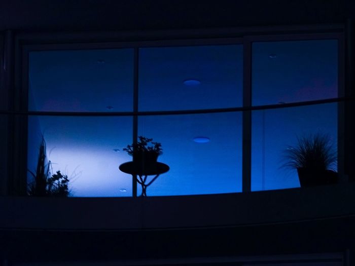 Silhouette person against blue sky seen through window