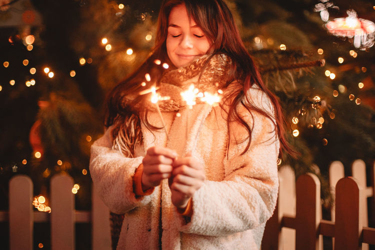 Young woman standing against illuminated christmas lights at night