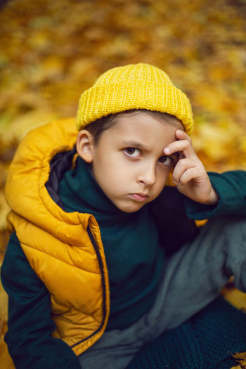 Portrait of a fashionable child boy autumn sitting on a trail in orange leaves in the afternoon