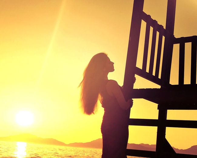Side view of silhouette woman standing on beach at sunset