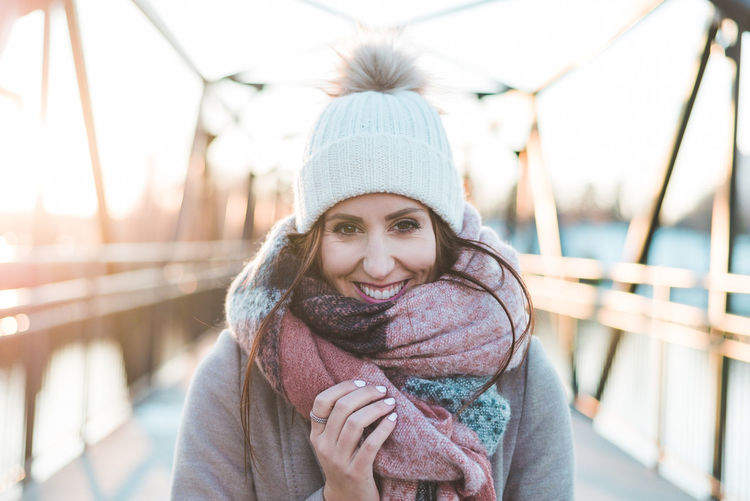 Portrait of smiling young woman wearing warm clothing on bridge