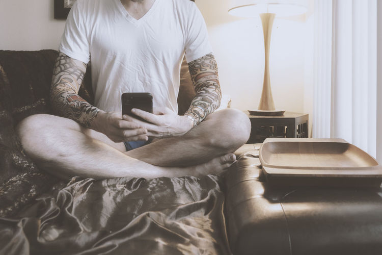 Person with tattoos sitting cross legged using a mobile phone indoor.s