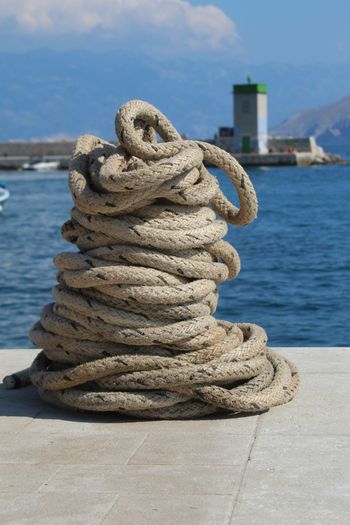 Close-up of rope tied to bollard at harbor against sky