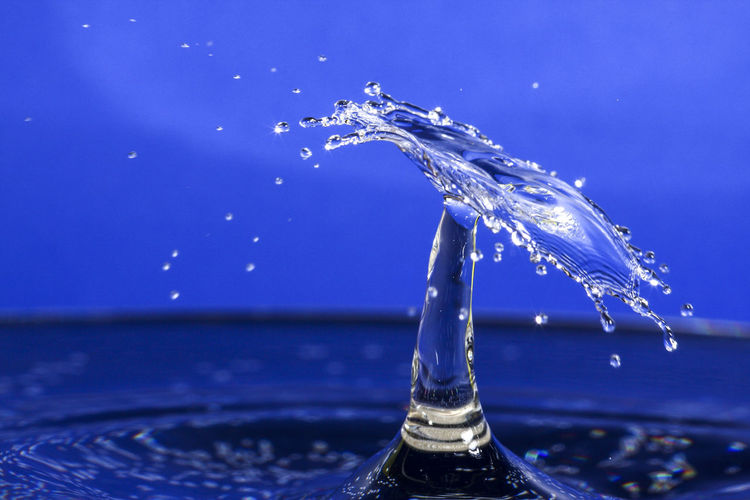 Close-up of drop splashing on water against blue background