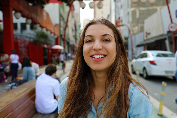 Portrait of smiling young woman against buildings in city