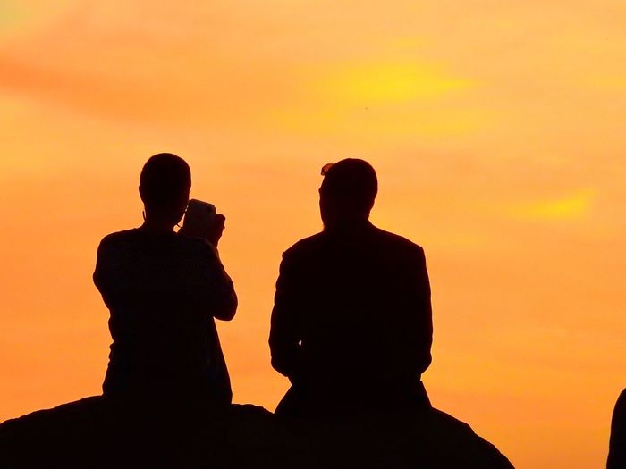 Silhouette men standing against orange sky