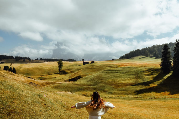 Rear view of woman standing on landscape against cloudy sky
