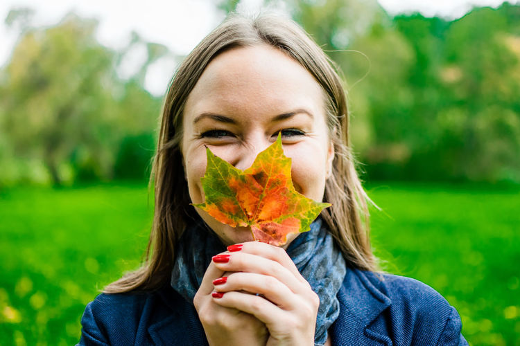 Portrait of young woman holding maple leaf at park