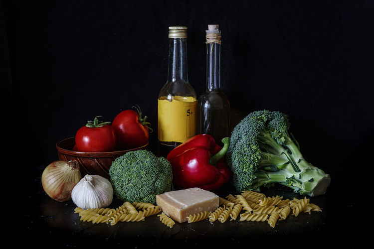 Still life, tomato, broccoli, oil and pasta on a black studio backgrou