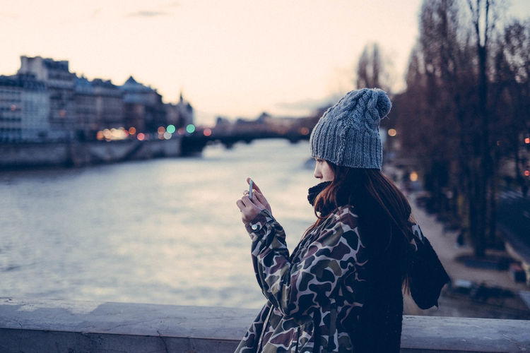 Side view of young woman photographing by seine river