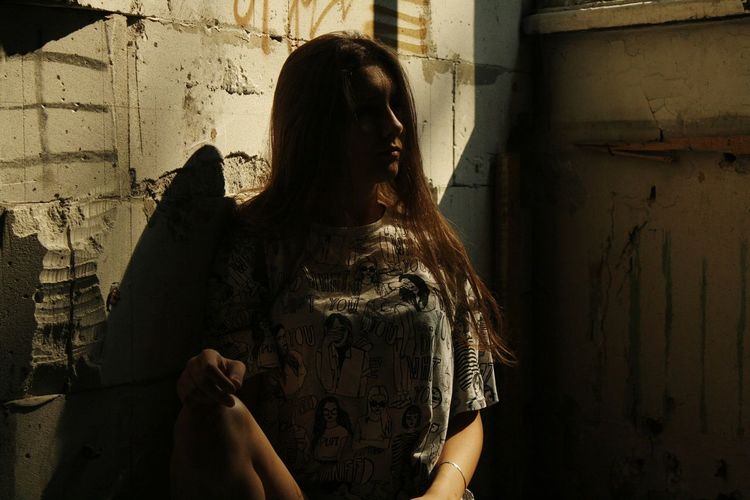Lonely woman sitting against wall in abandoned building