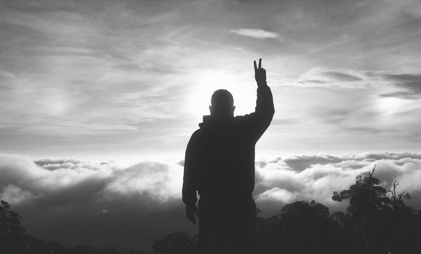 Silhouette man gesturing while standing on mountain against sky