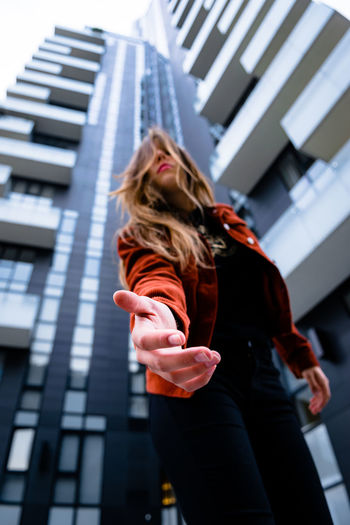 Low angle view of young woman standing against buildings in city
