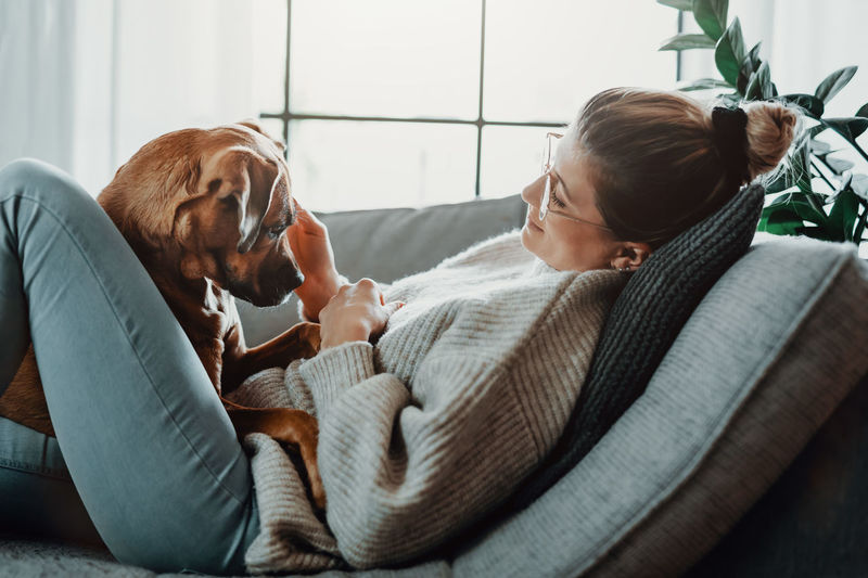 Woman with dog relaxing on sofa at home