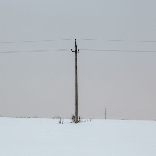 Electricity pylon on snow covered field against sky
