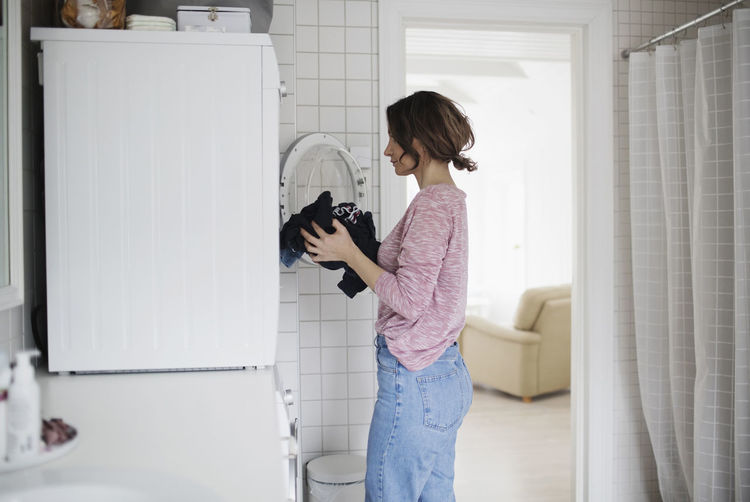 Side view of woman loading clothes in washing machine at home