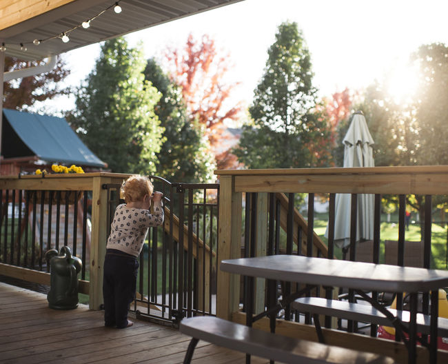 Toddler boy looks out gate on deck into backyard