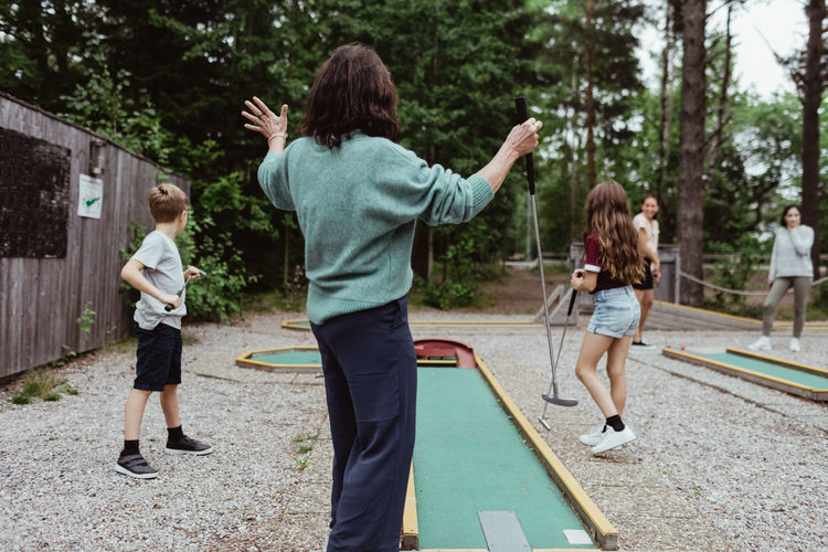 Rear view of woman playing miniature golf with family in backyard