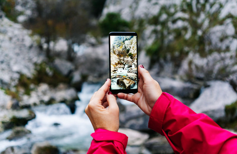 Bright photo of mountain waterfall and turquoise lake flowing into river on smartphone in hand on crop unrecognizable tourist in peaks of europe, asturias, spain