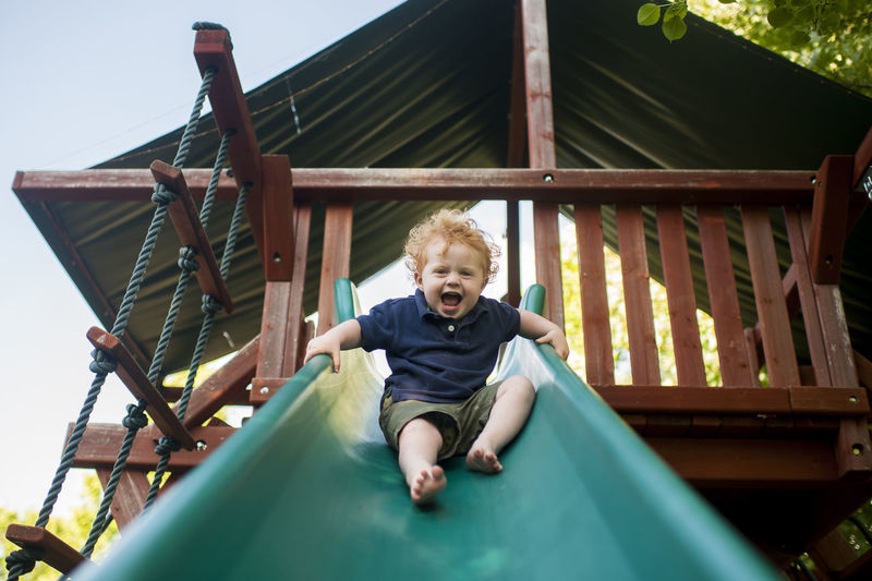 Low angle portrait of happy baby boy screaming while sliding at yard