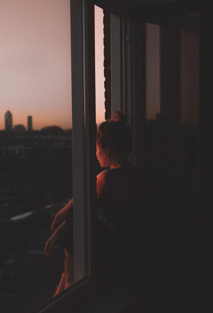 Side view of thoughtful depressed woman looking through window at sunset