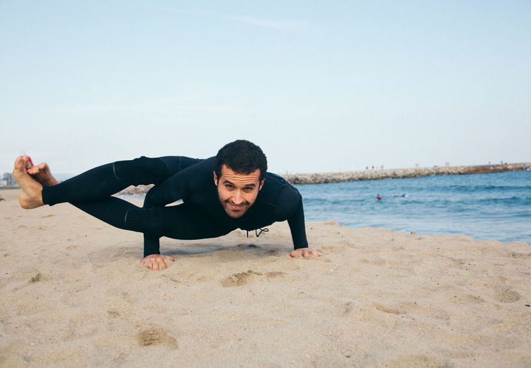 Man doing yoga on beach against sky