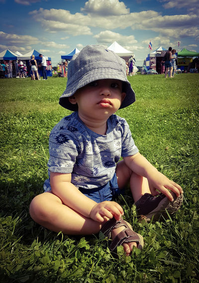 Cute boy sitting on field against sky