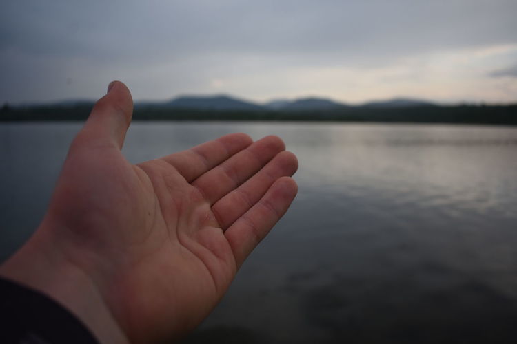 Cropped image of person against lake against sky