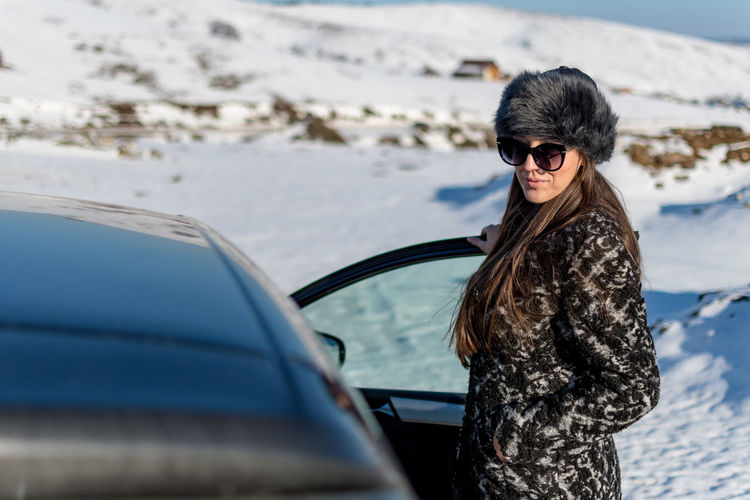 Portrait of woman standing by car on snow covered land