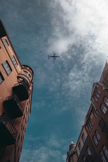 Low angle view of airplane flying over buildings against sky