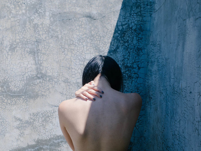 Rear view of topless woman standing against wall