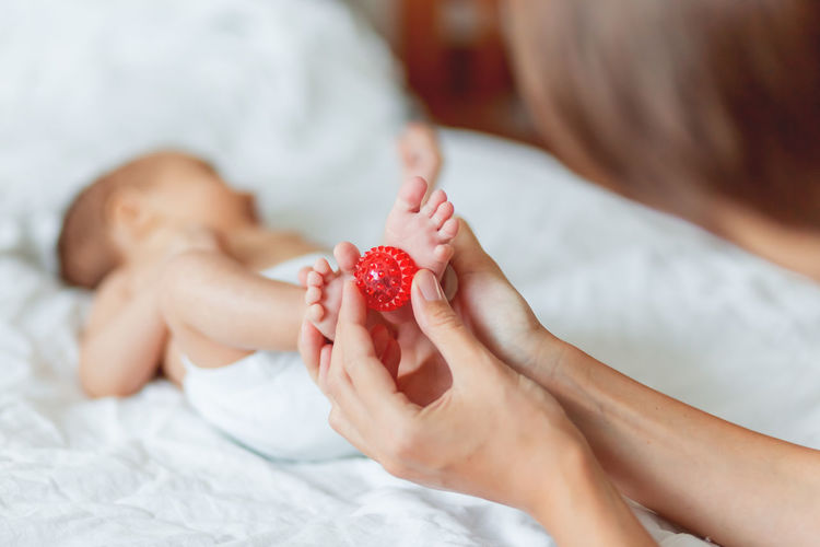 Mother holds newborn baby's feet. tiny fingers and red massage ball in woman's hand. cozy morning