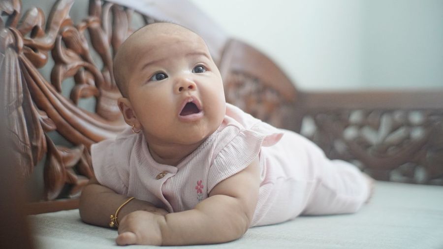 Cute baby girl lying on bed at home