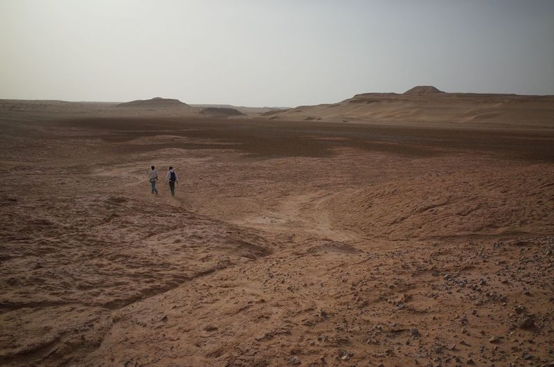 Distance view of man and woman walking at desert against sky