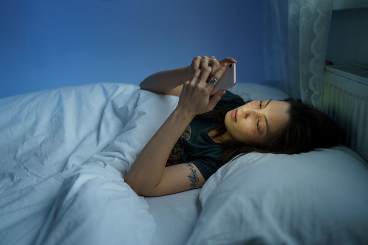 Woman suffering from internet addiction disorder, insomnia. female using smartphone in bed at night
