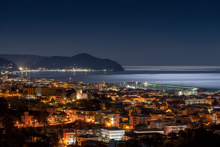 High angle view of illuminated city by sea against sky