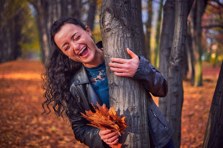 Young woman smiling while standing on tree trunk in forest