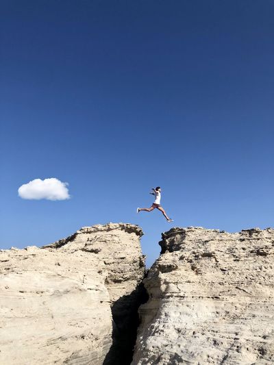 Low angle view of person jumping on rock against blue sky