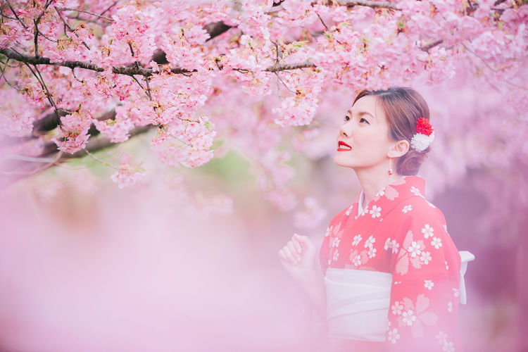 Low angle view of woman standing by pink cherry blossom