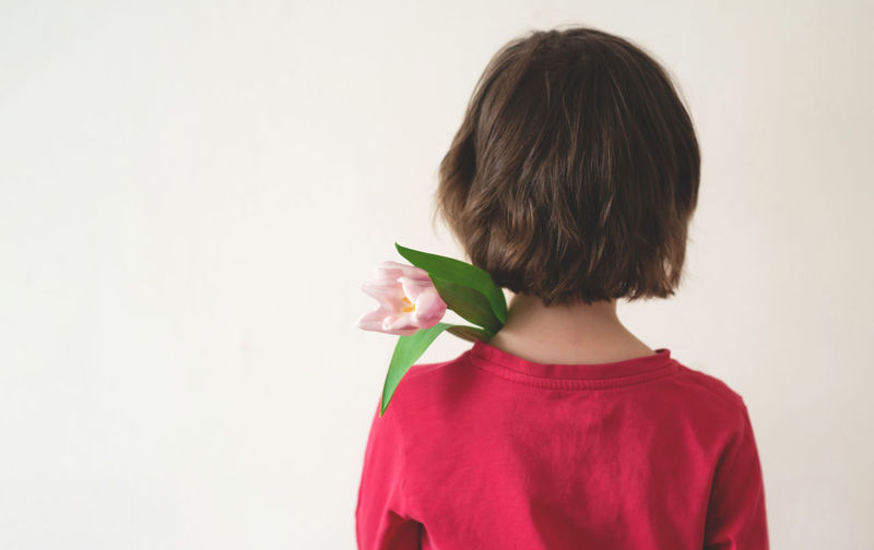 Rear view of young woman holding red rose against white background